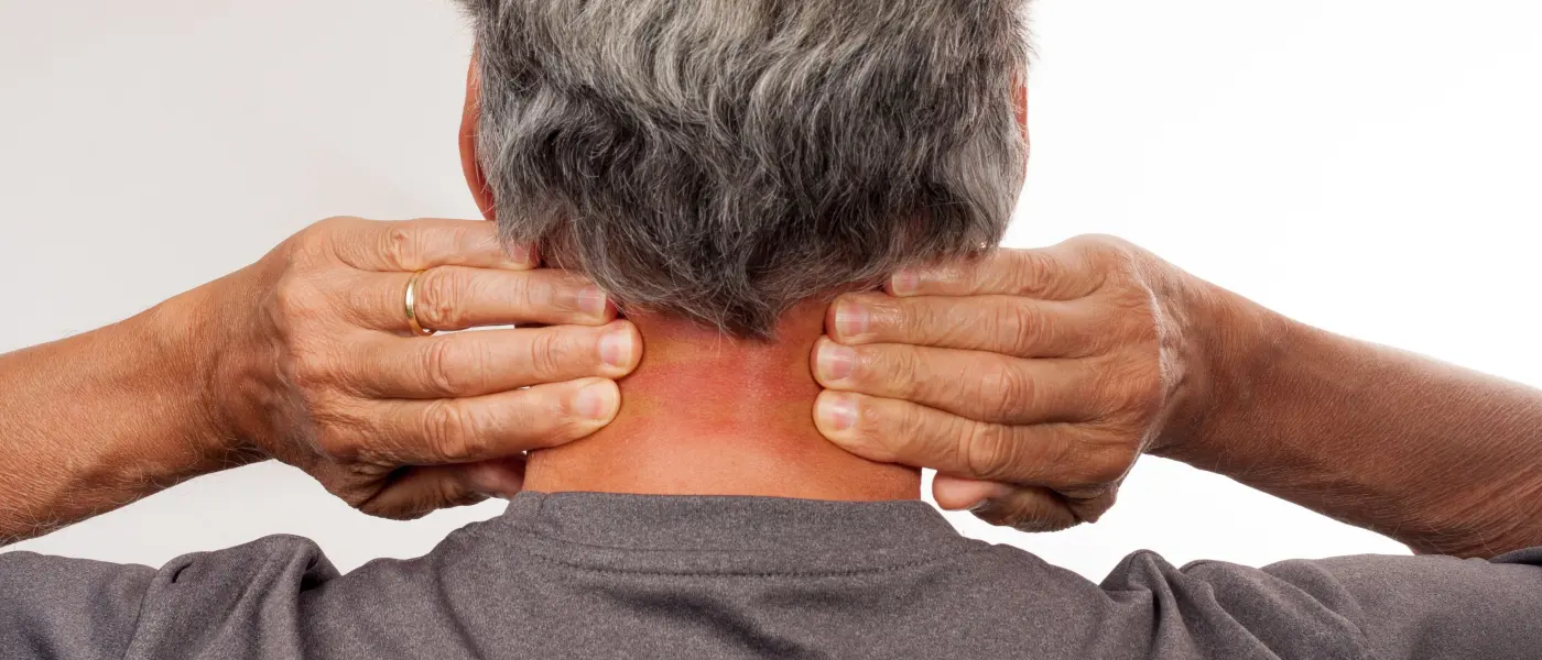 Man holding the back of his neck, with the base of the neck highlighted where a pinched nerve is felt
